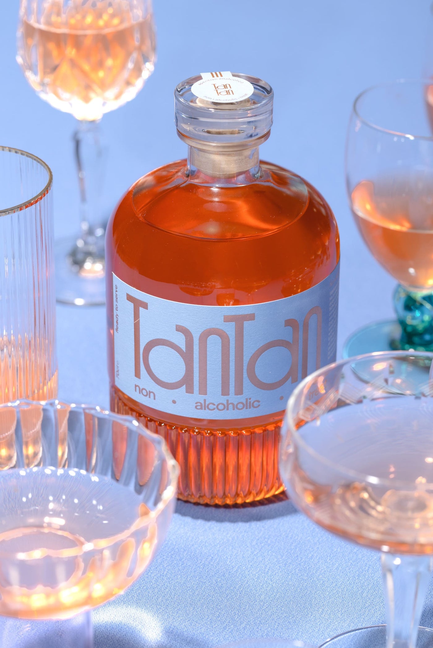 Bottiglia e bicchieri TANTAN su sfondo azzurro — still life aperitivo analcolico